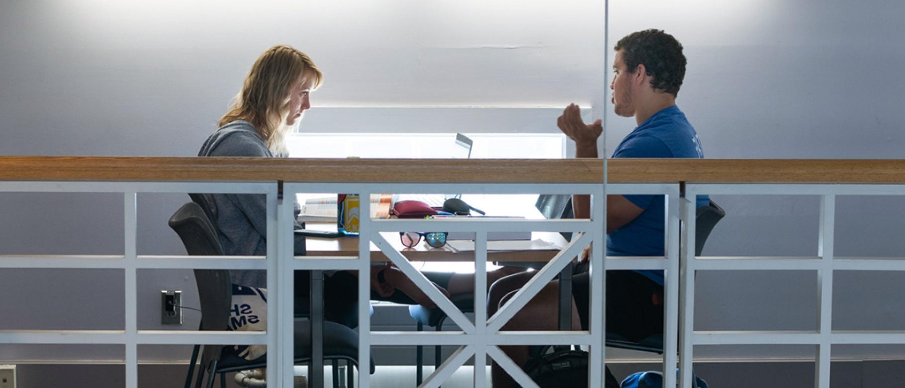 Two students talk while sitting in the Portland Campus library