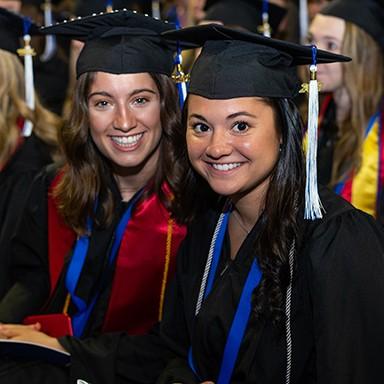 Two College of Arts 和 科学 undergraduate students sitting together at their commencement ceremony